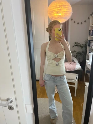 Vit festtopp med silverdetaljer och öppen rygg - Trendig beige halterneck topp med två dekorativa snäckor framtill och snygga cut-outs. Toppens material känns stretchigt och mjukt, perfekt för att skapa en cool och modern look. Passformen är tight och toppen är ärmlös.