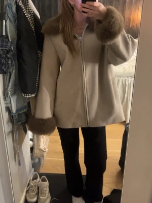 Beige kappa med fuskpälsdetaljer - Snygg beige kappa, med fluffiga bruna fuskpälsdetaljer vid krage och ärmslut. 🤎