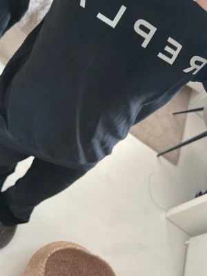Svart sweatshirt från Replay - Säljer en svart sweatshirt från Replay med stor vit logga framtill. Tröjan har rund halsringning och en liten metallbokstav 'R' vid halsen. Perfekt för en avslappnad och stilren look.