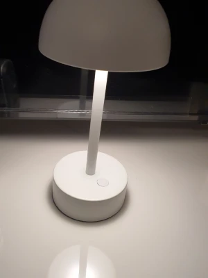 Vit bordslampa i modern design - Säljer en stilren vit bordslampa med rund fot och halvkupolformat lampskärm. Lampan har en enkel knapp på foten och mäter cirka 28 cm i höjd. Passar perfekt som skrivbordslampa eller mysbelysning. Tillverkad i metall och plast. Uppladdningsbar