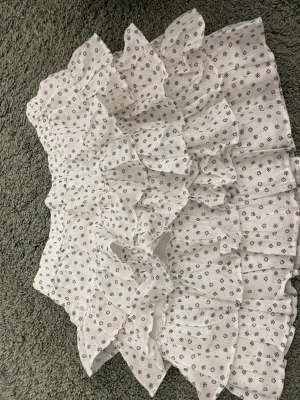 Vit volangkjol med småblommigt mönster - Supersöt vit kortkjol med volanger och små blommor över hela tyget. Kjolen har en luftig känsla och elastisk midja, perfekt för en fräsch och somrig look. Passar perfekt till en enkel topp eller stickad tröja.