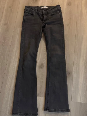 Svarta bootcut jeans med låg midja - Säljer ett par svarta bootcut jeans med låg midja och klassisk femficksdesign. Jeansen har en lätt utsvängd passform nertill och är tillverkade i stretchigt denimtyg för en bekväm känsla. Perfekta för dig som gillar en trendig och avslappnad look.