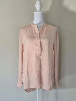 Aprikos blus i storlek S från ICONA - Fin kvalitet. Ny. V-ringning med sprund och dold knapp. Lång ärm med sprund och knapp. Längre bak än fram. Material 100 % polyester. Midjebredd ca 51 cm och längd ca 67-75 cm. 1204/70