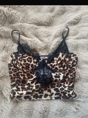 Leopardmönstrad spets tröja  - Snygg tröja med leopardmönster och tunna axelband. Dekorerad med svart spets längs kuporna och framtill för en extra detalj. Mjuk och stretchig känsla, perfekt för dig som gillar djurmönstrat. 