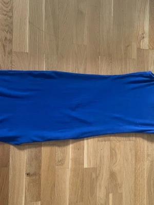 Blå långklänning i stretchigt tyg - En enkel och stilren blå långklänning i ett mjukt och stretchigt material. Klänningen har en rak passform och är ärmlös, perfekt för dig som gillar minimalistisk stil. Passar till många olika tillfällen och är lätt att styla med accessoarer.