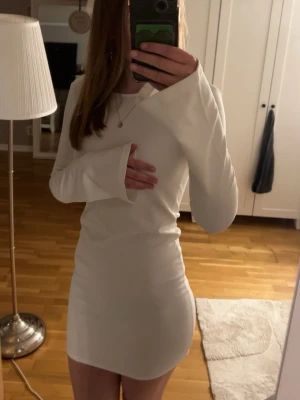 Vit långärmad klänning - Snygg vit klänning med långa ärmar och trendiga utsvängda ärmslut. Klänningen har en djup rygg med knytband upptill för extra detalj. Perfekt för dig som gillar stilrena och enkla plagg med en twist. Det finns två fläckar som jag inte försökt ta bort, tro det går bort i tvätten 
