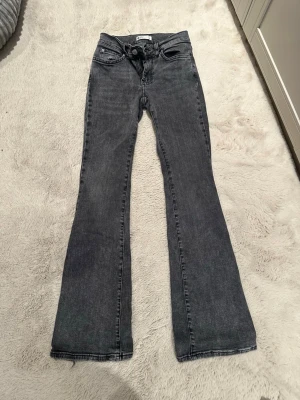 Grå bootcut jeans från Gina Tricot - Snygga grå bootcut jeans från Gina Tricot med klassisk femficksmodell och normalhög midja. Jeansen har en lätt utsvängd passform nedtill och är tillverkade i denim med en mjuk känsla. Perfekta för en trendig och avslappnad stil. Har inte använt på ett långt tag, har ba legat i garderoben :)