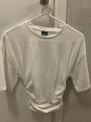 Tshirt ginatricot - Snygg vit t-shirt från Gina Tricot i storlek XXS med croppad passform och skrynkligt tyg på sidorna. Är helt oanvänd, jag vill sälja tröjan för att den är för liten för mig och det är ett litet hål på ena sidan i midjan som inte alls syns när man har på sig tröjan och lätt går att sy igen🤍