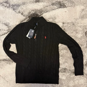 Polo Ralph Lauren Black Cable-Knit Quarter-Zip Sweater - Size Medium - NWT - Elevate your wardrobe with this timeless Polo Ralph Lauren cable-knit sweater in classic black. Crafted with precision, this quarter-zip piece features the iconic red pony embroidery for a touch of sophisticated prep. 🧥 Perfectly versatile for layering or wearing on its own, it’s a must-have staple for any gentleman’s collection.  • Brand: Polo Ralph Lauren • Condition: Brand new with tags (NWT) 🏷️ • Features: Classic cable-knit pattern with a quarter-zip neckline and leather pull. • Detail: Icon