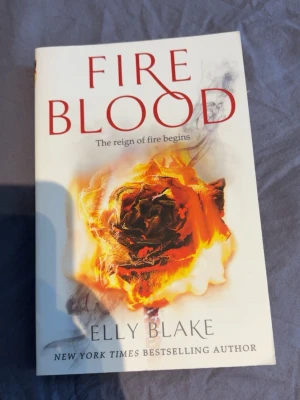Fireblood av Elly Blake - Fireblood är en fantasyroman av Elly Blake med ett omslag i vitt och rött, prytt av en brinnande ros. Boken är på engelska och handlar om Ruby som måste rädda två kungadömen där is och eld är i krig. Perfekt för dig som gillar magi, äventyr och spänning.