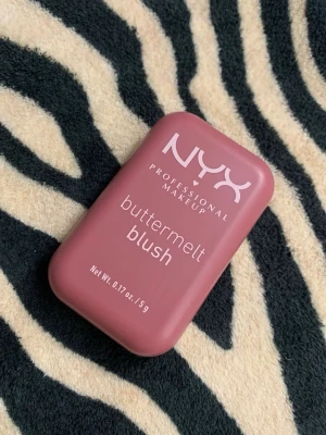 NYX Buttermelt Blush For The Butta - NYX Buttermelt Blush i nyansen 'For The Butta' är ett puderrouge i en mjuk, matt rosabrun färg. Kommer i en smidig, rektangulär plastförpackning som är lätt att ta med. Perfekt för att ge kinderna en naturlig och fräsch look.