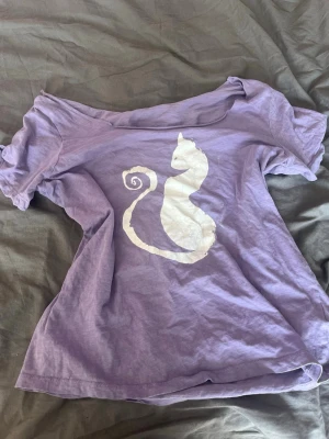 Gullig lila t shirt med katt tryck - Halsirngen är klippt för en offshoulder look! Trycket har försvunnit men annars i bra skick!