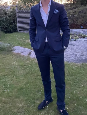 Mörkblå kostym från Oscar Jacobson - Snygg mörkblå kostym från Oscar Jacobson med klassisk kavaj och matchande byxor. Kavajen har två knappar, fickor med lock och bröstficka. 