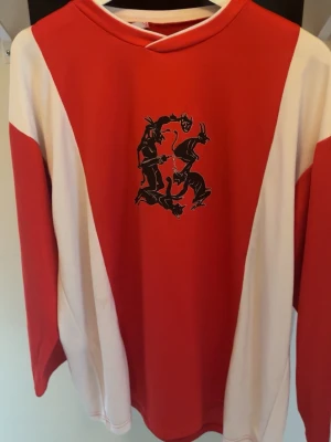 Röd långärmad Yung Lean & Sad Boys tee - Unik röd och vit långärmad t-shirt från Yung Lean & Sad Boys med svart tryck av två figurer på bröstet. Oversized fit och sportig look, perfekt för dig som gillar streetwear och vill sticka ut. Tillverkad i mjuk bomull för skön känsla.
