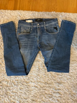 Blå slim fit jeans från REPLAY - Snygga blå slim fit jeans från REPLAY med klassisk femficksdesign och diskreta slitningar framtill. Jeansen har raka ben och detaljerade bakfickor med broderi. Tillverkade i mjuk denim med stretch för extra komfort.