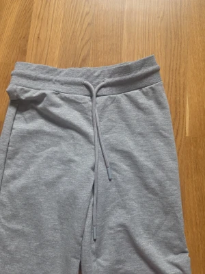 Grå mjukisbyxor med raka ben - Snygga grå mjukisbyxor med raka ben och dragsko i midjan. Byxorna har en enkel och clean design, perfekta för en chill och avslappnad stil. Tillverkade i mjukt och bekvämt material som känns skönt mot huden.