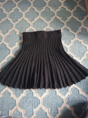 Svart plisserad stickad kjol - En svart, kort plisserad kjol i stickat material. Kjolen har hög midja och ett mjukt, stretchigt tyg som ger en snygg siluett. Perfekt för dig som gillar en klassisk men trendig look.