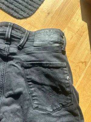 Svarta Replay jeans  - Snygga svarta jeans från Replay med klassisk femficksdesign och raka ben. Jeansen har en diskret logga på bakfickan och patch med Replay-märke i midjan. Tillverkade i bomull med lite stretch för extra komfort.