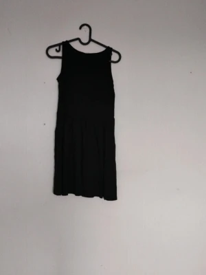 Svart ärmlös kortklänning - Klassisk svart ärmlös kortklänning med rund halsringning och lätt utställd kjol. Enkel och stilren design som ger en tidlös look. Perfekt för dig som gillar minimalistiska plagg.