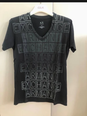 Svart Armani Exchange t-shirt - Snygg svart t-shirt från Armani Exchange med grafiskt tryck framtill i rutmönster och text. T-shirten har v-ringning och korta ärmar. Perfekt för dig som gillar stilrena plagg med en twist. Tillverkad i mjuk bomull för skön känsla. Sommar T-shirt 