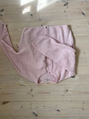 Ljusrosa kofta från Gina Tricot  - Mysig ljusrosa kofta från Gina Tricot premium med rund halsringning och knappar framtill. Koftan är stickad i ett fluffigt material och har långa ärmar samt ribbade muddar vid ärmslut och nederkant. Perfekt för lager-på-lager-stil.