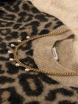 Guldhalsband med pärldroppar - Snyggt halsband i guldfärgad metall från Los Angeles Atelier. Kedjan har sju droppformade pärlor som hänger längs framsidan och ger en elegant touch. Perfekt accessoar för att lyfta vilken outfit som helst.