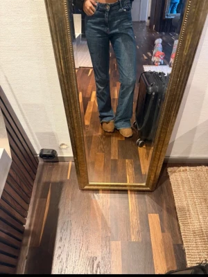 Blå bootcut jeans med hög midja - Säljer ett par klassiska blå bootcut jeans med hög midja och raka ben. Jeansen har fem fickor och stängs med dragkedja och knapp. Perfekta till sneakers eller boots för en avslappnad men snygg look. 