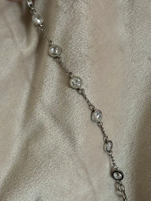 Silverfärgat armband med zirkoner - Stilrent armband i silverfärgad metall med runda, infattade zirkoner längs hela kedjan. Pärlorna är klara och ger ett elegant intryck, perfekt för att lyfta vilken outfit som helst. Lätt att matcha med andra smycken och har en tunn kedja mellan pärlorna.