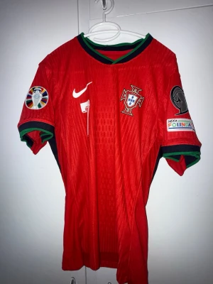 Portugal Ronaldo #7- Player version/- Röd matchtröja  - Säljer en riktigt snygg Portugal Ronaldo nummer 7 Player Version  i röd färg. Samma typ av material tröja som spelarna använder på match tunnare, lättare och mer figursydd än supporter-versionen. Köpt på jearseyzone Detaljer:  * Lag: Portugal national football team * Spelare: Cristiano Ronaldo * Nummer: 7 * Version: Player Version / Pro Version * Färg: Röd * Material: Lätt och ventilerande matchmaterial * Passform: Slim/athletic fit * Skick: Mycket fint skick, som oanvänt   Storlek M, slim fit 