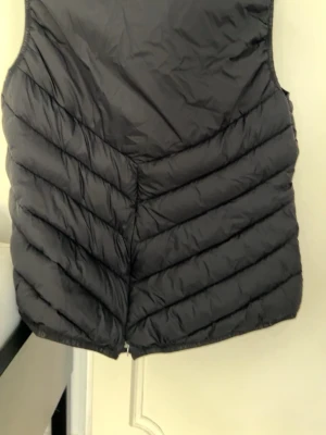 Svart dunväst från Fairfield - Snygg svart dunväst från Fairfield med klassisk quiltad design och dragkedja. Västen har en stilren look och är perfekt för lager-på-lager. Tillverkad i lätt och värmande material med diskreta detaljer.