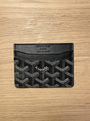 Svart kortfodral  - Snyggt svart kortfodral från  med klassiskt mönster i vitt och grått. Tillverkat i läder med flera kortfack och präglad logotyp upptill. Perfekt för dig som vill ha en stilren och exklusiv accessoar i fickan.