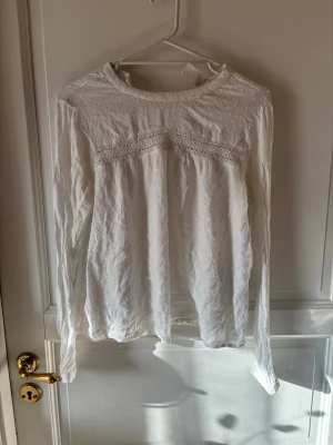 Vit blus med spetsdetaljer - Söt vit blus med långärmad design och rund halsringning. Blusen har fina spetsdetaljer över bröstet och diskret prickmönster upptill. 