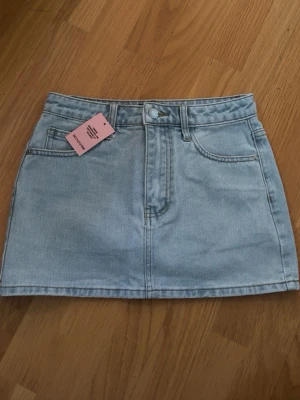 Ljusblå jeanskjol med fickor - Trendig ljusblå jeanskjol i kort modell med klassiska fickor fram och bak.