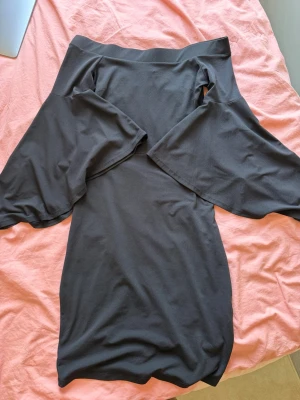 Svart offshoulder klänning från Gina Tricot  - En svart klänning med offshoulder-design och långa ärmar. Klänningen har en enkel och stilren look, perfekt för dig som gillar minimalistisk stil. Materialet känns mjukt och följsamt mot kroppen.