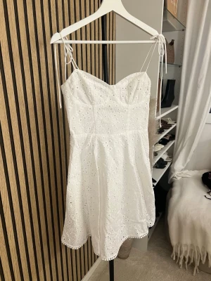 Vit broderad sommarklänning med knyt - Söt vit kortklänning med broderade detaljer och tunna axelband med knyt. Klänningen har en lätt utsvängd passform och är perfekt för varma dagar. Tillverkad i bomull för en luftig känsla. Skriv om ni vill ha bild på 🫶🏼🫶🏼