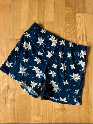 Blommiga blå shorts med resårmidja - Mörkblå shorts med vitt blommönster och elastisk midja. Perfekta för varma dagar och har en avslappnad passform. Tillverkade i mjukt material som känns skönt mot huden.