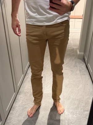 Beige jeans från J.Lindeberg - Snygga beige jeans från J.Lindeberg med klassisk femficksdesign och diskret logotyp på bakfickan. Byxorna har normal passform och är tillverkade i mjuk bomull som ger en skön känsla. Perfekta för dig som vill ha en stilren look. Modell: Jay Storlek: 31/34