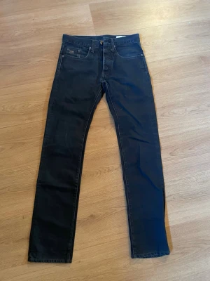 Blåa jeans från G-Star - Säljer ett par blåa jeans från G-Star med klassisk femficksdesign och diskret logga på bakfickan. Jeansen har raka ben och normal midja, perfekta för en clean och stilren look. 