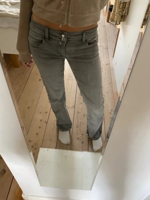 Grå jeans med stjärndetalj - Säljer ett par grå jeans med normal passform och en silverfärgad stjärna på bakfickan. Jeansen har klassisk femficksdesign och raka ben. Perfekta för dig som vill ha en unik detalj på dina jeans. Storlek 164