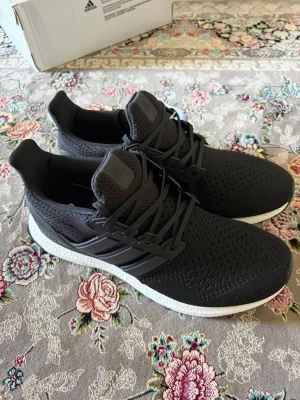 Adidas Ultraboost sneakers - Snygga svarta Adidas Ultraboost sneakers med stickad ovandel i mesh för bra andningsförmåga. Skorna har klassiska tre ränder på sidan, svart snörning och en vit, responsiv Boost-sula som ger grym komfort. Perfekta för dig som gillar stilrena och sportiga sneakers.
