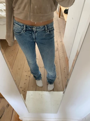 Låg midjade jeans med broderade fickor - Säljer ett par ljusblå bootcut jeans med snygga broderade detaljer på bakfickorna. Jeansen har låg midja och klassisk femficksdesign. Perfekta för dig som gillar en avslappnad men ändå trendig look.