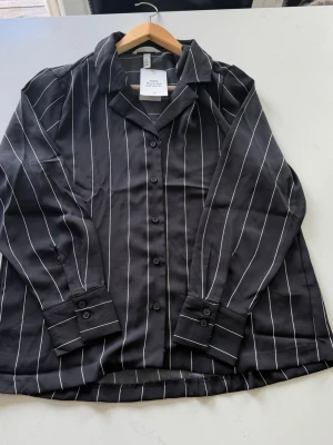 Svart randig skjorta från HM - H&M Randig Skjorta – Aldrig använd med lapp kvar! 🏷️ Säljer denna snygga skjorta från H&M i storlek S (EUR S). Mörkgrå/svart med vita ränder – ett tidlöst mönster som passar till allt. Plagget är helt oanvänt med original-lappen kvar, i nyskick! 🔹 Märke: H&M  🔹 Storlek: S  🔹 Material: 100% Recycled Polyester  🔹 Skick: Nyskick – lapp kvar ✅  🔹 Nypris: 299 kr → Säljer för 149 kr Frågor? Skriv gärna! Frakt tillkommer. 📦