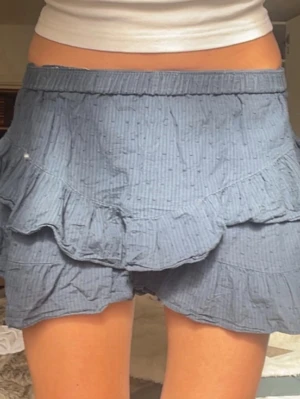 Blå volangkjol från Meet Me There - Blå kortkjol från Meet Me There med volangdetaljer, resår i midjan och inbyggda shorts. Perfekt för sommardagar☀️💕