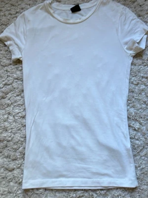 Vit basic t-shirt från Gina Tricot - En klassisk vit t-shirt från Gina Tricot i storlek XS. T-shirten har rund halsringning och korta ärmar. Tillverkad i mjuk bomull som känns skön mot huden. Perfekt att matcha med jeans eller kjol för en enkel och clean look.