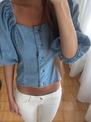Denim puffärmad blus med knappar - En jättesöt blus i denim-look med puffärmar och täckta knappar framtill. Den är aldrig använd därmed perfekt skick.