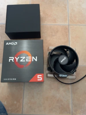 AMD Ryzen 5 processor med kylare - AMD Ryzen 5 processor från 5000-serien med tillhörande originalkylare. Processorn levereras i sin svarta och gråa kartong och kylaren har svart plastfläkt och metallflänsar. Perfekt för gaming eller uppgradering av datorn.