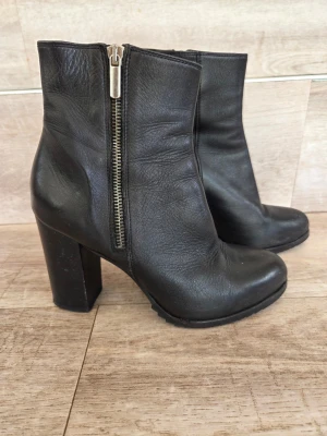 A pair Svarta stövletter med klack och dragkedja - Säljer ett par svarta boots  i skinn med grov klack och markerad sula. Bootsen har en snygg silverfärgad dragkedja på sidan och rundad tå. Perfekta för dig som vill ha en edgy look till hösten eller vintern. Klackhöjd ca 8 cm