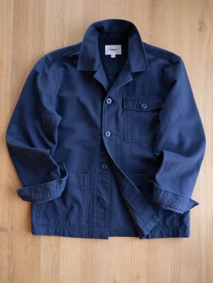 Mörkblå overshirt från Dobber, size S - Stilren mörkblå overshirt från Dobber i kraftig bomull. Klassisk krage, knappstängning framtill och en bröstficka med lock och knapp. Perfekt lager på lager-plagg med avslappnad passform och snygga detaljer.