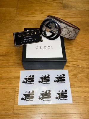 Gucci beige GG Supreme bälte - Säljer ett klassiskt Gucci GG Supreme bälte i beige med brunt GG-mönster och stor silverfärgad logospänne. Bältet är gjort i skinn och har detaljer i syntet. Perfekt accessoar för att lyfta din outfit.