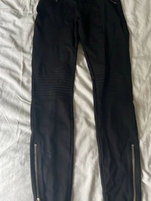Svarta leggings med dragkedjor - Snygga svarta leggings med coola detaljer som ribbade partier över knäna och dragkedjor vid bensluten. Tight passform och stretchigt material som sitter skönt. Perfekta för en trendig och edgy look. använt några gånger.